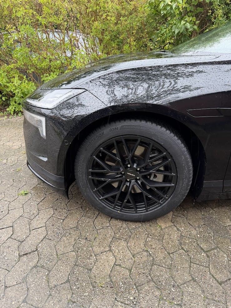 Close-up of black rims on a black car, parked on paving stones.